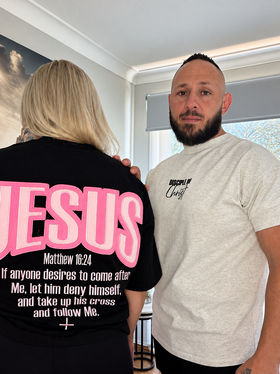 Couple wearing Jesus Deny Yourself oversized Christian tees, front view with pink and black JESUS print | WORDOFGOD Apparel
