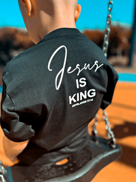Child on a swing wearing a black Jesus Is King kids tee, back view | WORDOFGOD Apparel